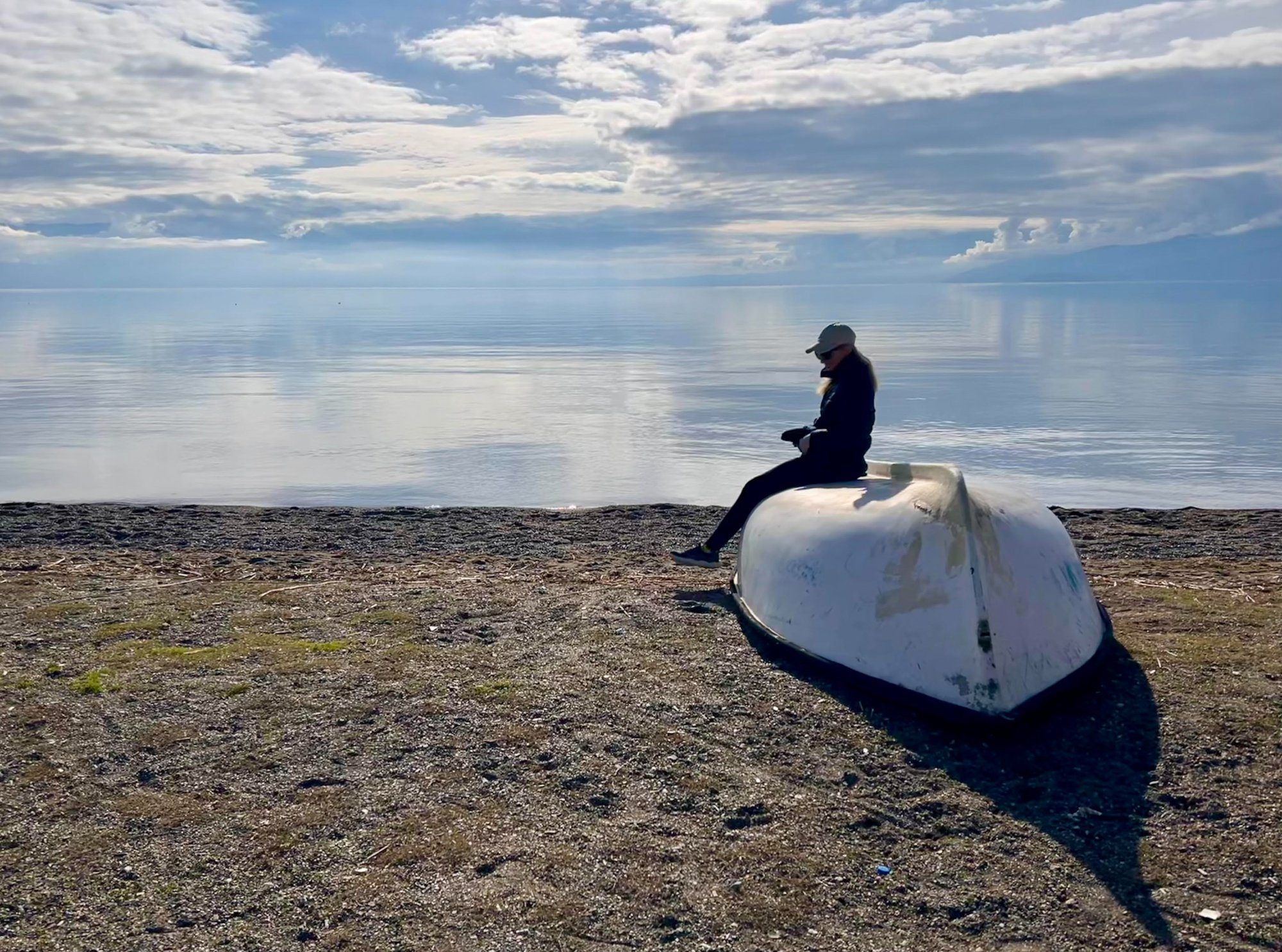 Person sitting on an overturned boat by the sea